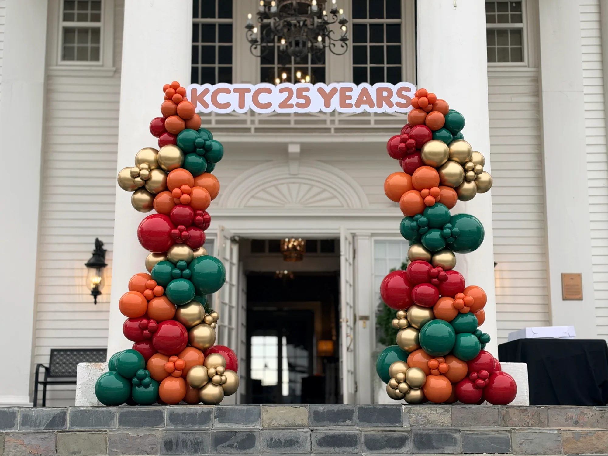 Two balloon columns in front of a mansion entrance holding a sign "KCTC 25 YEARS"